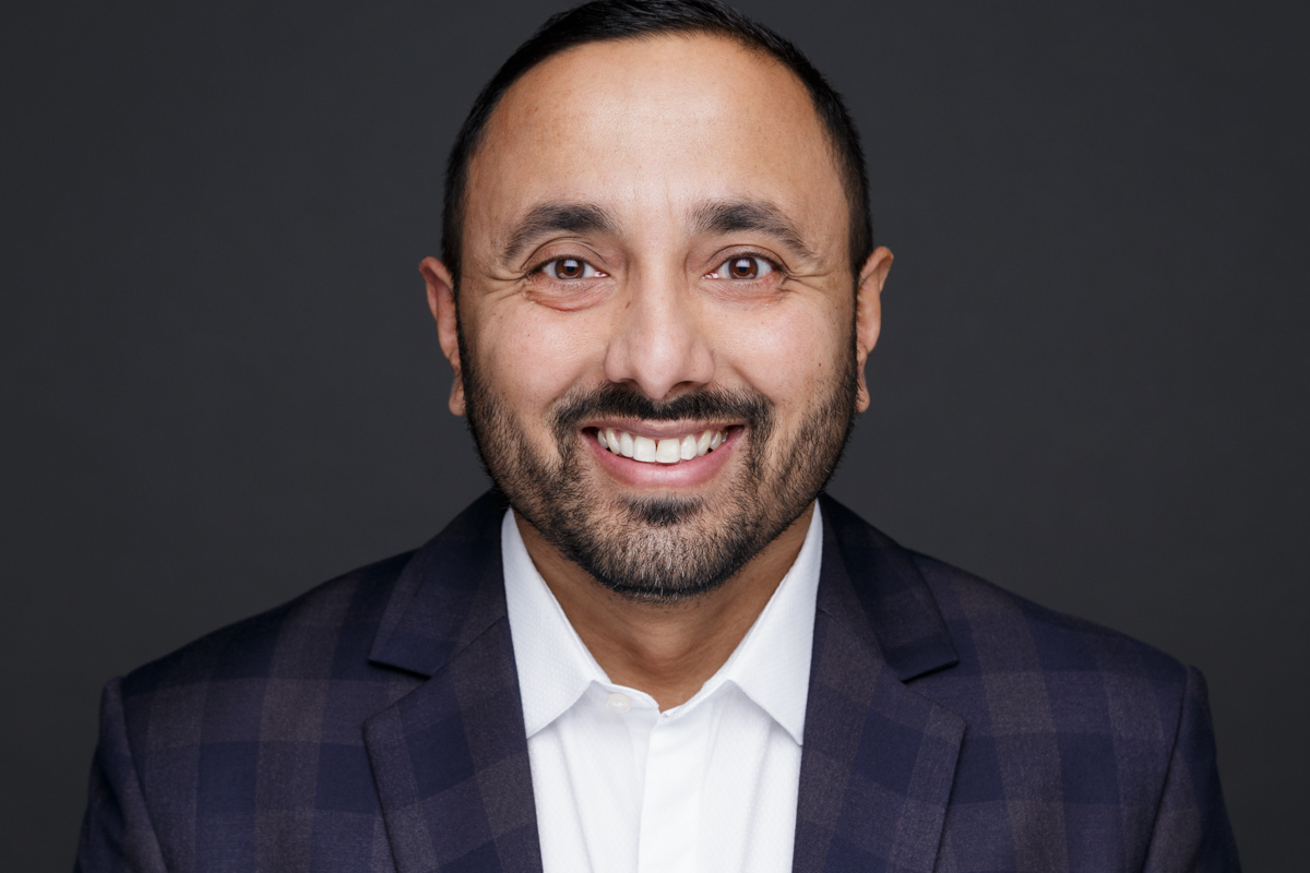 Divesh wears a white shirt smiling at the camera against a black back drop