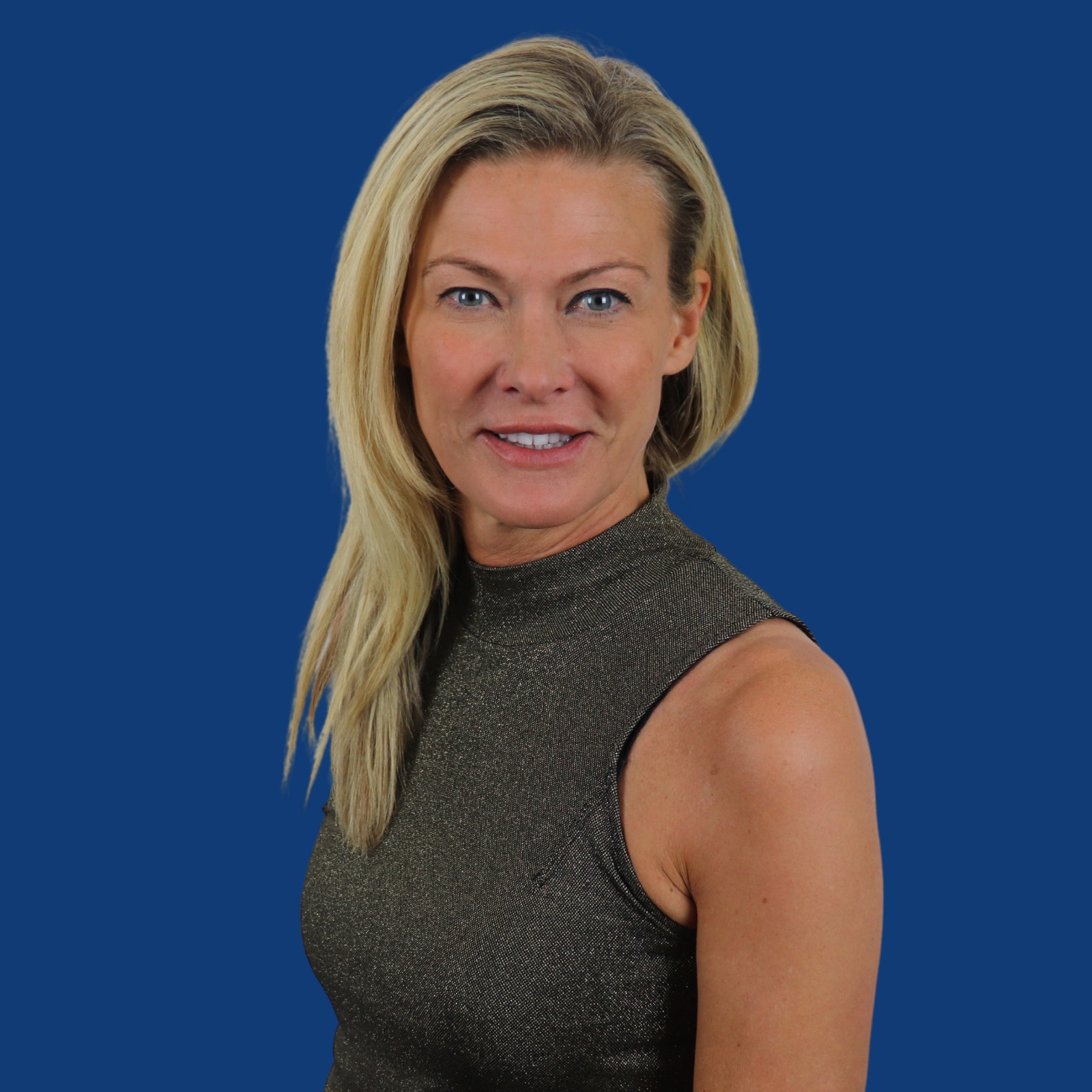 Amanda stands side on looking to the camera in front of a blue background. She is wearing a grey dress and her hair is down. 