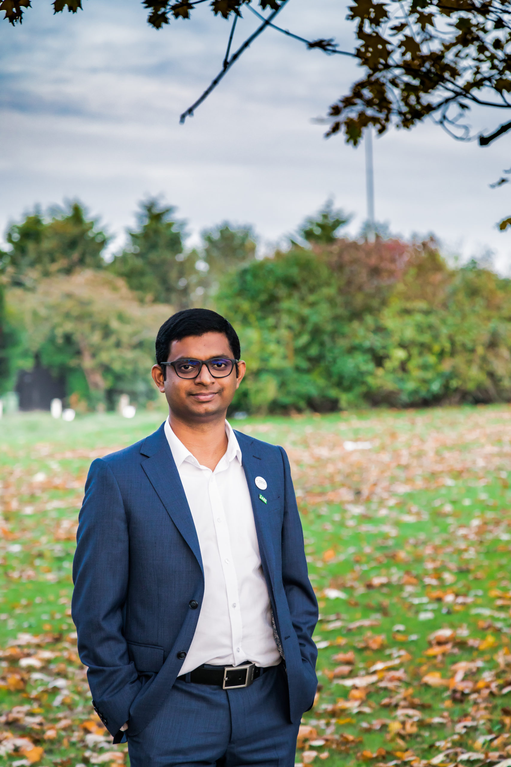 Issac stands in blue suit in front of an open green field