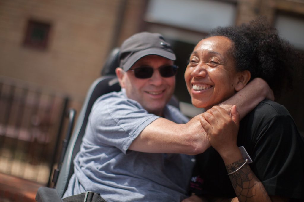 A man is hugging his carer outside a brick building