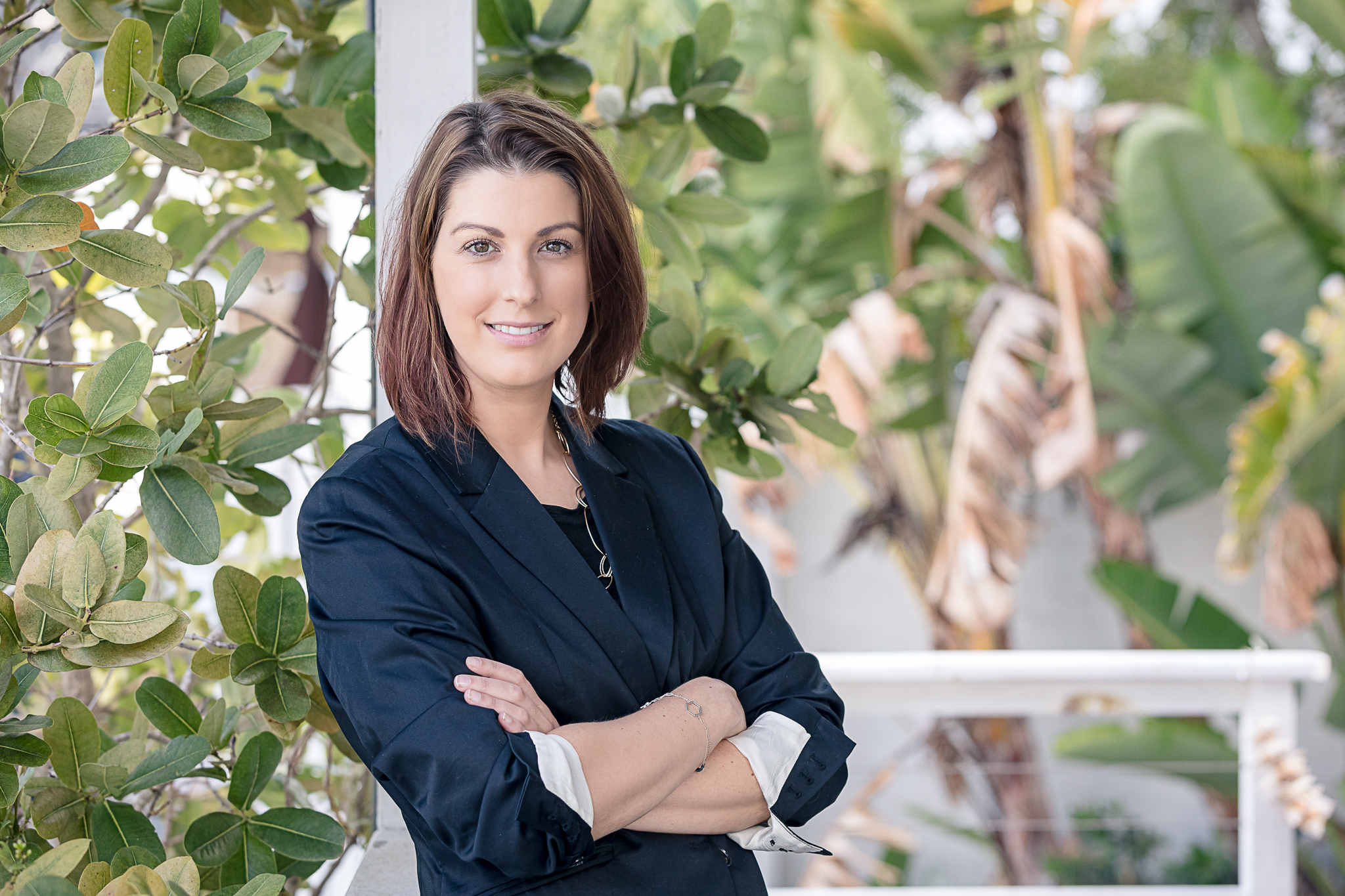 Tarrryn stands side on to the camera smiling, in front of a tree and white fence