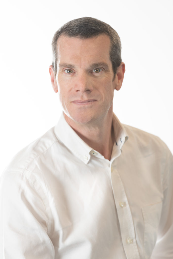 Jonathan looks into the camera, wearing a white shirt against a white backdrop