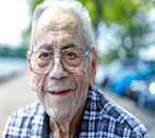 Older man with glasses looks into the camera outside.