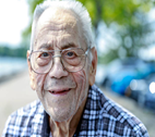 Older man with glasses looks into the camera outside. 