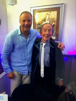 Derek smiling at the camera with an older man in a tie.