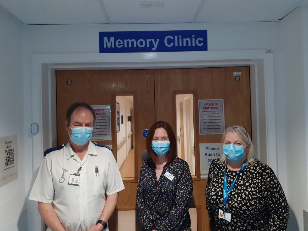 Three individuals stand outside the memory clinic, wearing face masks. 