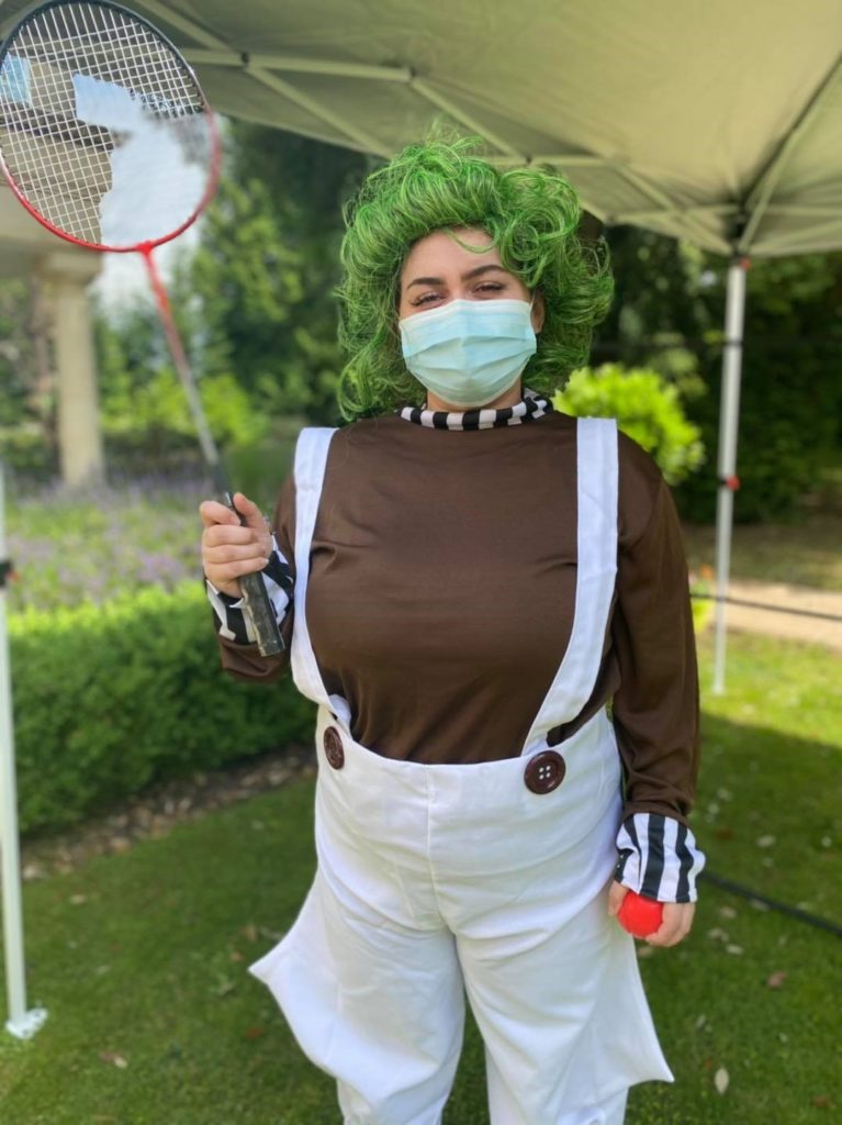 Care worker is facing the camera at a garden party wearing a mask dressed as an oompa loompa